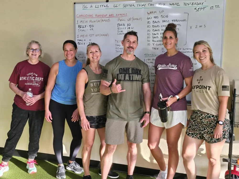 Billy Anderson with a group of Waypoint Fitness clients in front of the gym whiteboard